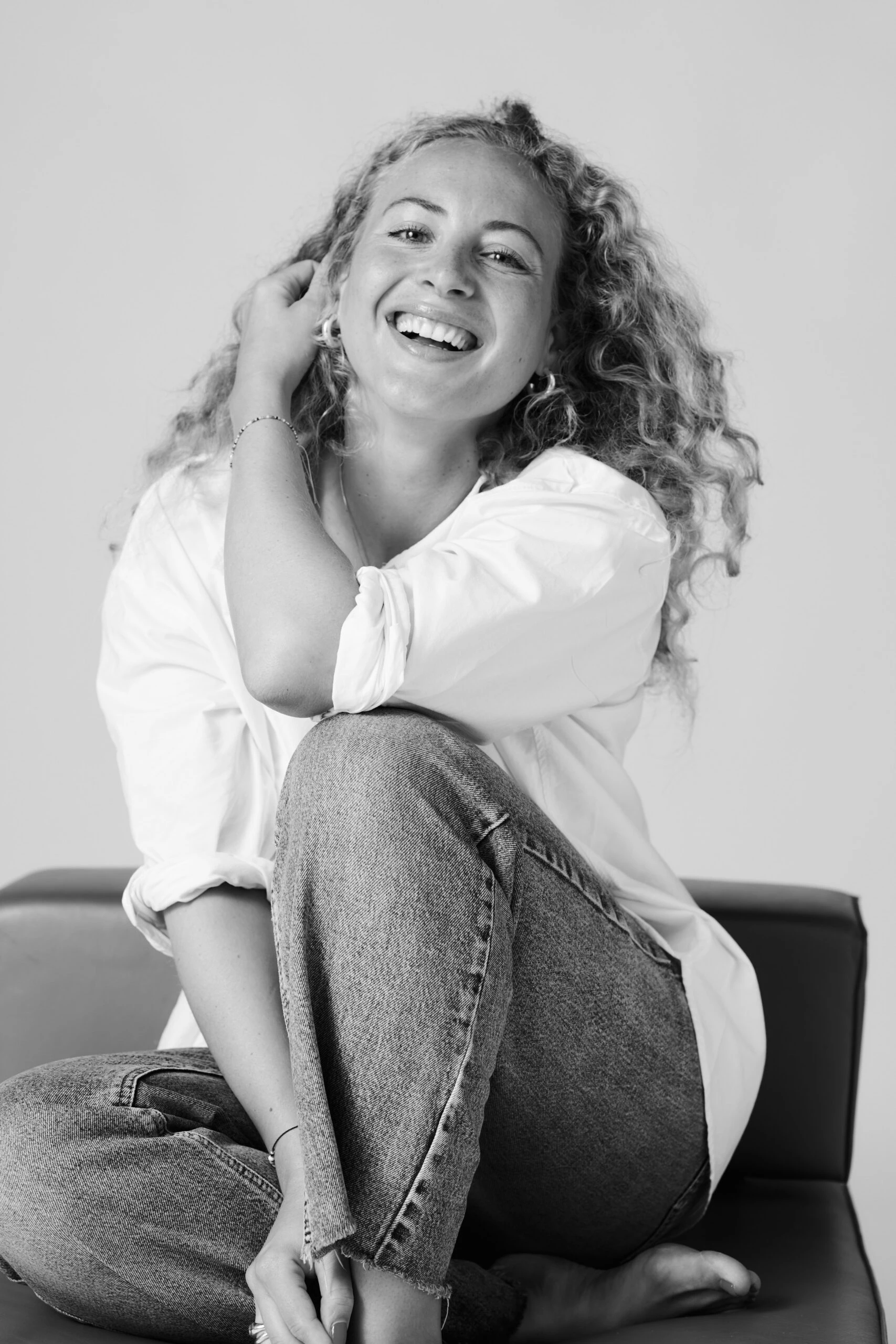 Schwarz-Weiß-Porträt von Leonie Voglmaier, lachend auf einem Sofa.
